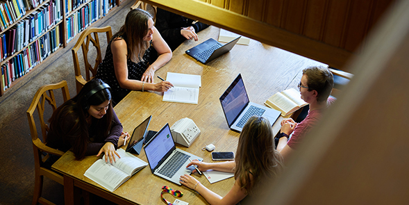 Students studying with laptops and books in a library.